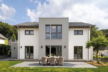 Außenansicht des FingerHaus-Musterhauses SENTO in Bad Vilbel mit moderner, symmetrischer Architektur, heller Putzfassade, großer Terrasse und gepflegtem Garten.
