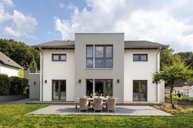 Außenansicht des FingerHaus-Musterhauses SENTO in Bad Vilbel mit moderner, symmetrischer Architektur, heller Putzfassade, großer Terrasse und gepflegtem Garten.
