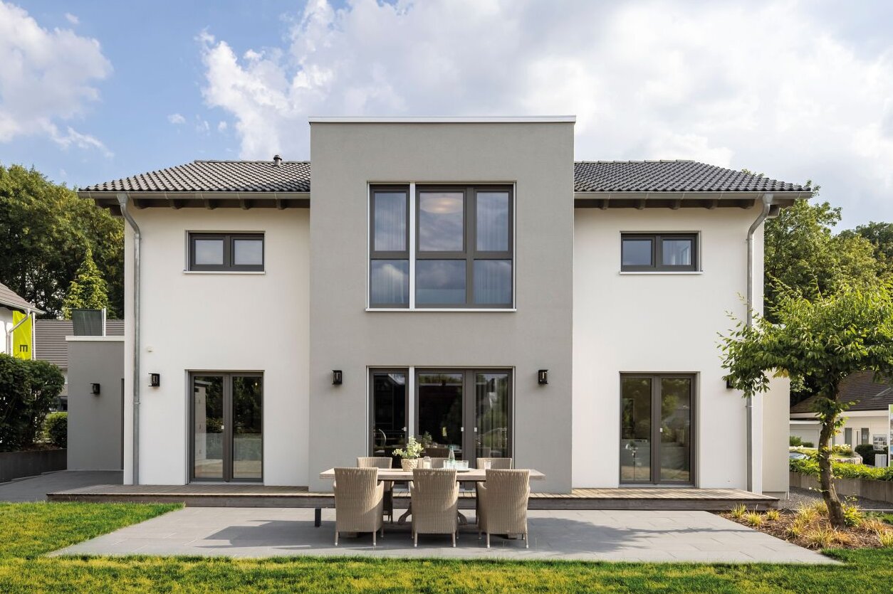 Außenansicht des FingerHaus-Musterhauses SENTO in Bad Vilbel mit moderner, symmetrischer Architektur, heller Putzfassade, großer Terrasse und gepflegtem Garten.