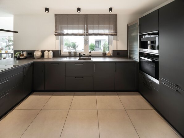 Moderne Küche im Musterhaus NEO in Wuppertal mit dunklen Einbauschränken, integrierten Elektrogeräten und stilvollem Design.