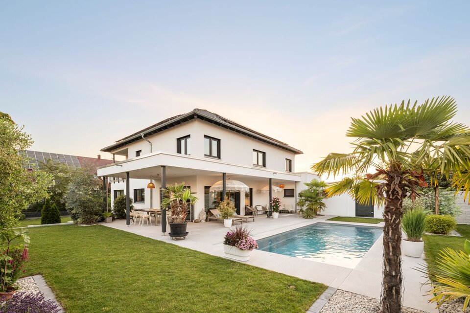 Außenansicht der frei geplanten FingerHaus Stadtvilla mit Pool, überdachter Terrasse, Rasenfläche und mediterran gestalteter Gartenanlage.