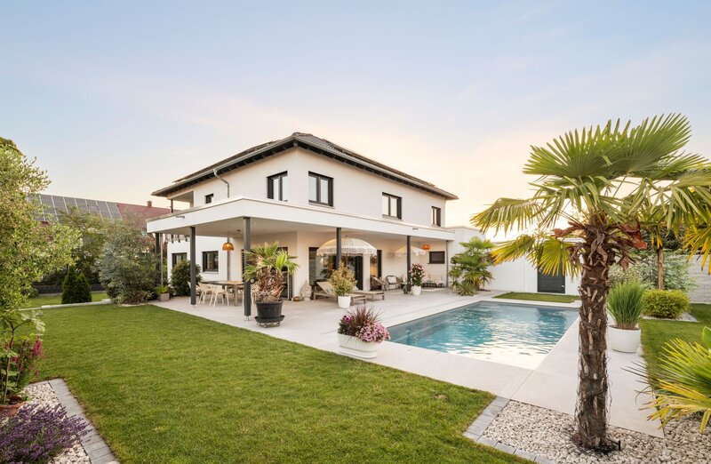 Außenansicht der frei geplanten FingerHaus Stadtvilla mit Pool, überdachter Terrasse, Rasenfläche und mediterran gestalteter Gartenanlage.