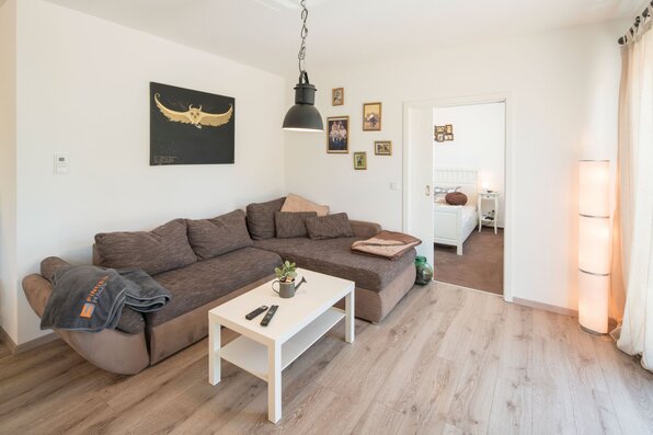 Gemütliches Wohnzimmer in einem frei geplanten Finger-Haus mit Ecksofa, Couchtisch, Wandbildern und Blick ins Schlafzimmer.