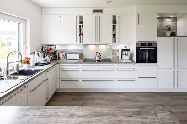 Moderne weiße Einbauküche mit viel Stauraum, großem Fenster und hochwertigen Geräten.