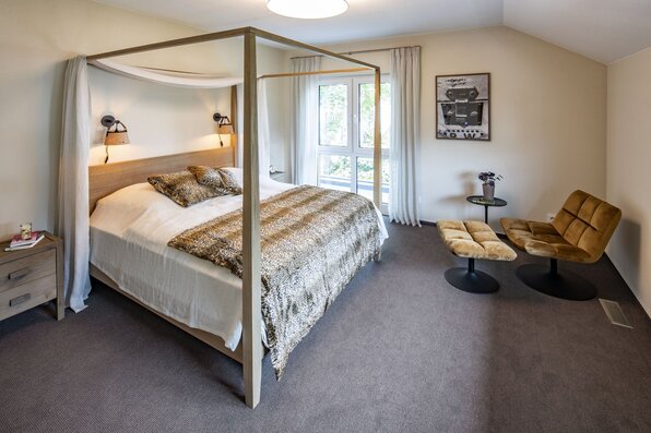 Schlafzimmer im MEDLEY Musterhaus Mannheim mit Himmelbett, gemütlicher Sitzecke und großen Fenstern.