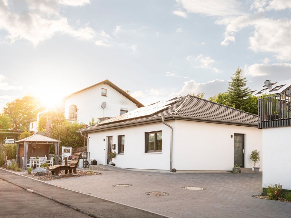 Außenansicht eines frei geplanten Kundenhauses mit Photovoltaikanlage auf dem Walmdach bei tief stehender Sonne.