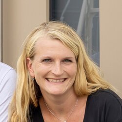 Fünfköpfige Familie sitzt gemeinsam auf den Stufen vor dem Hauseingang eines weißen Einfamilienhauses.