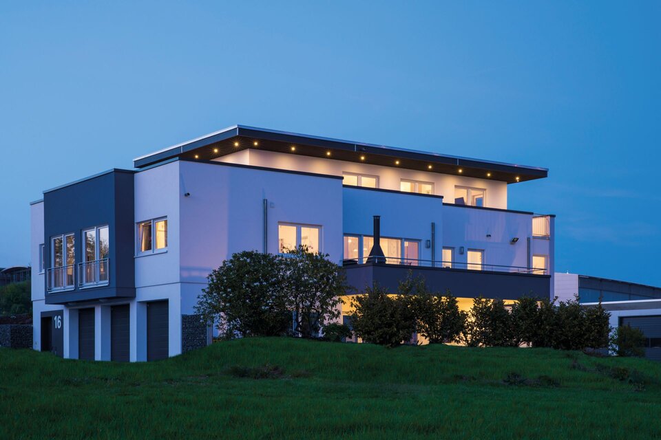 Frei geplantes FingerHaus mit moderner Architektur und Flachdach, abends beleuchtet und von der Gartenseite aufgenommen.