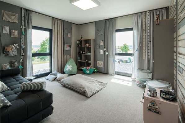 Kinderzimmer im Musterhaus ALTERO in Gießen mit kreativer Wandgestaltung, Spielbereich und viel Tageslicht durch große Fenster.