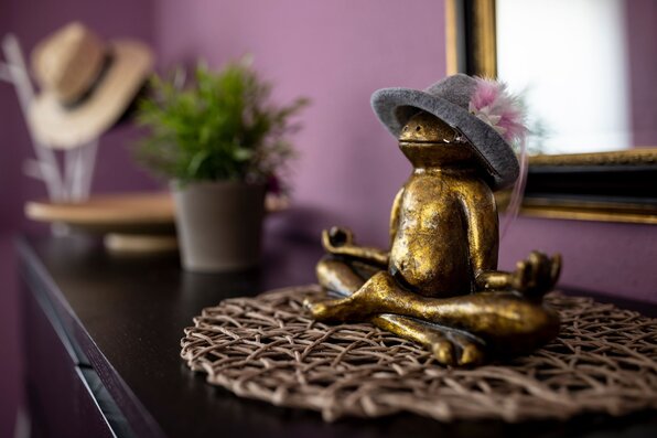 Dekorative goldfarbene Froschfigur mit Hut auf einer Kommode vor violetter Wand und Spiegel im Hintergrund