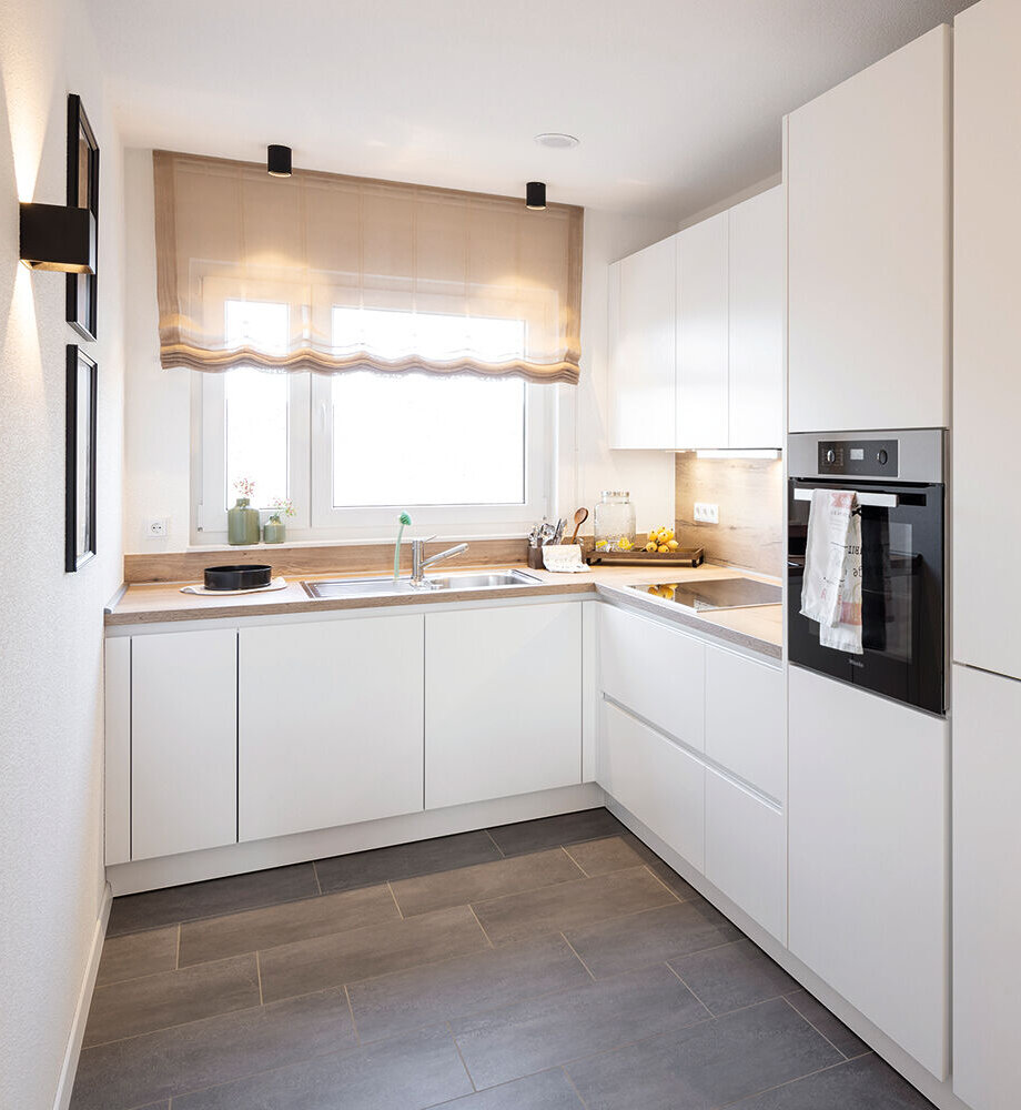 U-förmige Küche mit weißen Fronten, Spüle am Fenster, hellen Wänden und modernen Elektrogeräten.