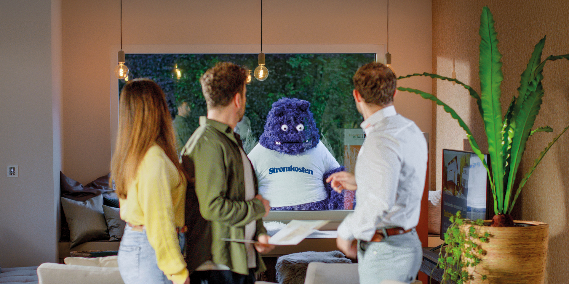 Drei Personen stehen in einem modern eingerichteten Wohnzimmer und blicken durch das große Fenster auf ein blaues, plüschartiges Wesen mit der Aufschrift „Stromkosten“ – Symbolfigur aus der FingerHaus-Kampagne „Das Unerwartete“.
