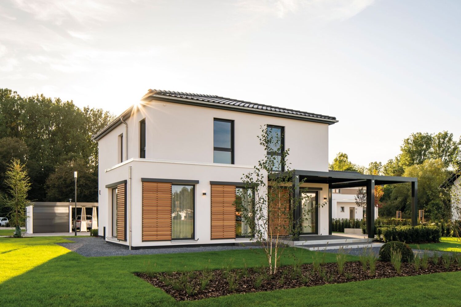 Außenansicht des Musterhauses MEDLEY 300 B im Musterhauspark Frankenberg mit Holzraffstores, überdachter Terrasse und gepflegtem Garten.