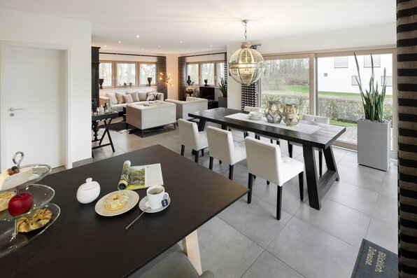 Offener Wohn-, Ess- und Kochbereich im Musterhaus NEO 312 in Bad Vilbel mit modernem Esstisch, großer Fensterfront und stilvollem Lounge-Bereich im Hintergrund.
