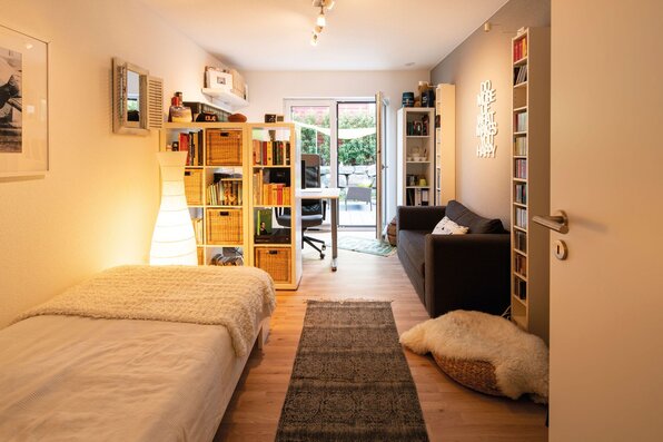 Gemütliches Gästezimmer in einem frei geplanten FingerHaus mit Einzelbett, Sofa, Bücherregal, Arbeitsplatz und Zugang zur Terrasse.