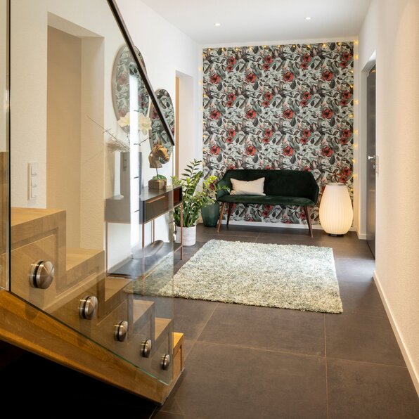 Moderner Flur in einem FingerHaus-Haus mit Glas-Treppengeländer, Akzentwand mit floralem Muster, grünem Teppich und eleganter Sitzbank.