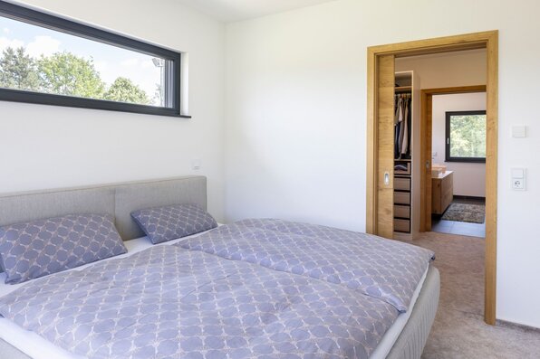 Helles Schlafzimmer mit Doppelbett, Durchgang zur Ankleide und weiterem Zugang zum Badezimmer.