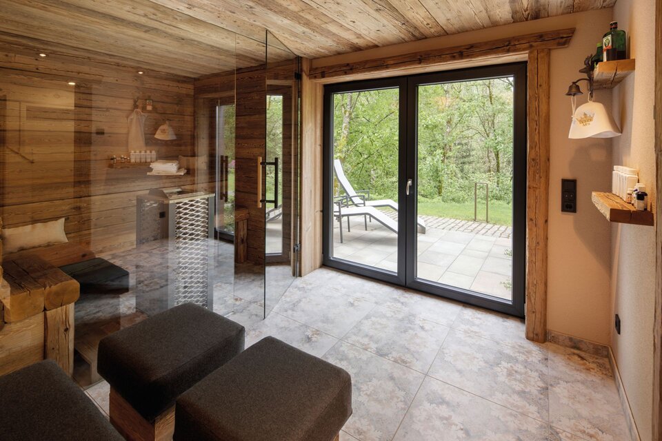 Gemütlicher Saunabereich in einem FingerHaus-Haus mit rustikaler Holzverkleidung, Glaswand und direktem Zugang zur Terrasse mit Blick in die Natur.