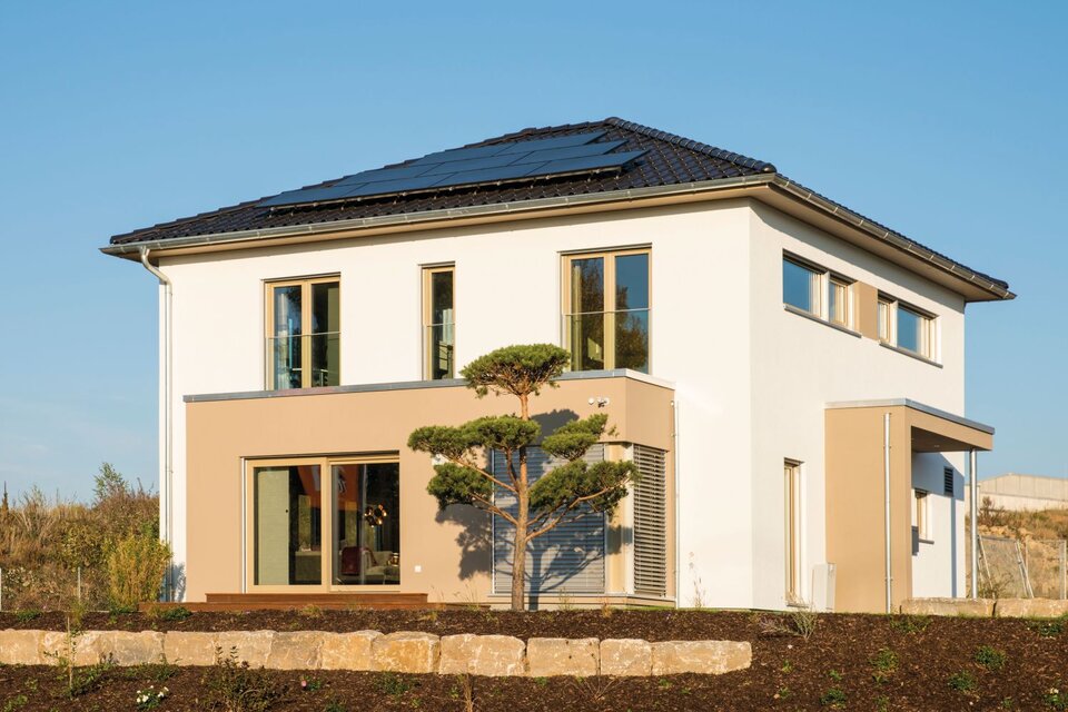 Musterhaus MEDLEY 300 B in Kassel bei Sonnenschein, mit klarer kubischer Architektur, großen Fensterflächen und markantem Baum im Vorgarten.