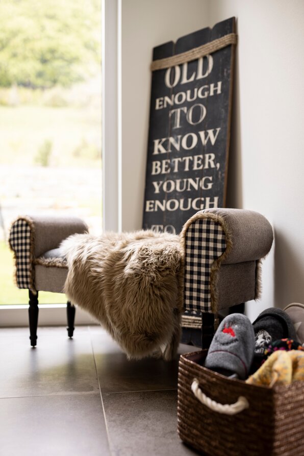 Gemütliches Flurdetail in einem FingerHaus mit rustikaler Bank, Fellauflage, Korb mit Hausschuhen und dekorativem Wandbild.
