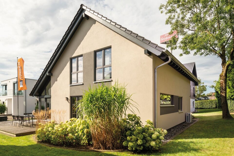 Musterhaus NEO in Wuppertal mit heller Putzfassade, großen Fenstern, gepflegtem Garten und angrenzender Terrasse mit Sitzgruppe.
