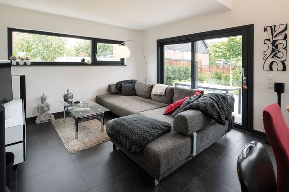 Modernes Wohnzimmer in einem FingerHaus-Einfamilienhaus mit großer Eckcouch, Glas-Couchtisch und Zugang zur Terrasse.