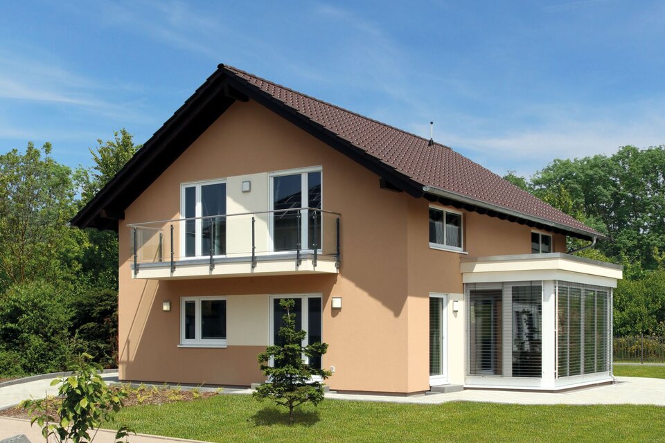 FingerHaus MEDLEY 310 – Musterhaus in Erfurt mit Satteldach, apricotfarbener Fassade und weißem Wintergartenanbau. Das Haus verfügt über einen Balkon mit Glasgeländer und einen gepflegten Garten mit Rasen und Gehweg