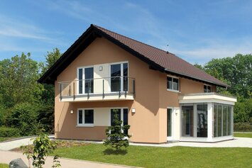 FingerHaus MEDLEY 310 – Musterhaus in Erfurt mit Satteldach, apricotfarbener Fassade und weißem Wintergartenanbau. Das Haus verfügt über einen Balkon mit Glasgeländer und einen gepflegten Garten mit Rasen und Gehweg