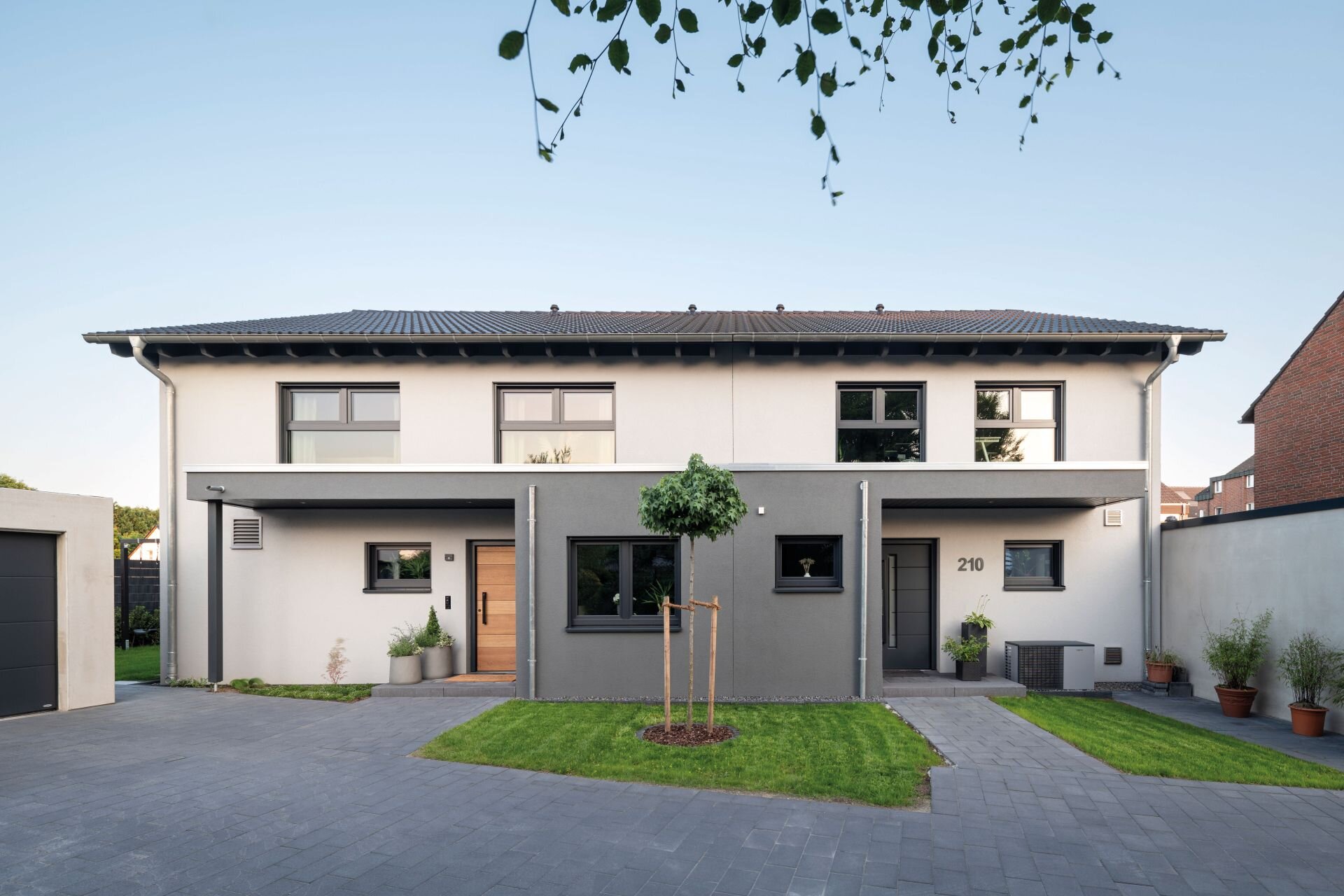 Doppelhaus mit Satteldach, zweifarbiger Putzfassade und zwei überdachten Eingangsbereichen mit Vorgarten