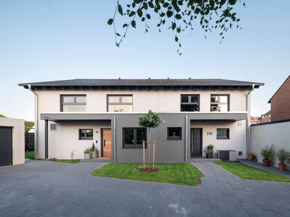 Doppelhaus mit Satteldach, zweifarbiger Putzfassade und zwei überdachten Eingangsbereichen mit Vorgarten