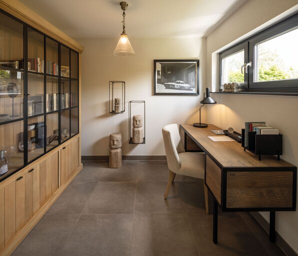 Modernes Homeoffice im FingerHaus NEO 300 Musterhaus Hannover mit Holzschreibtisch, Glasvitrine und dekorativen Elementen.