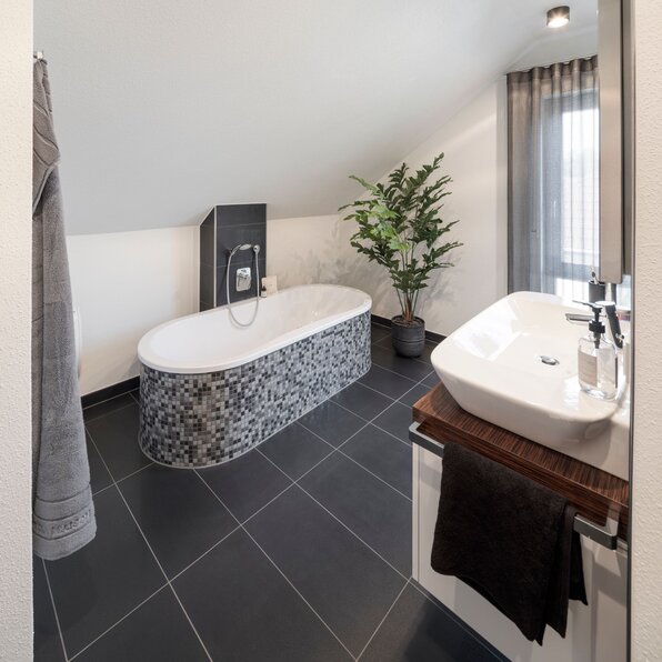 Modernes Badezimmer im frei geplanten FingerHaus Musterhaus Marburg mit Badewanne in Mosaikoptik und Waschtisch.