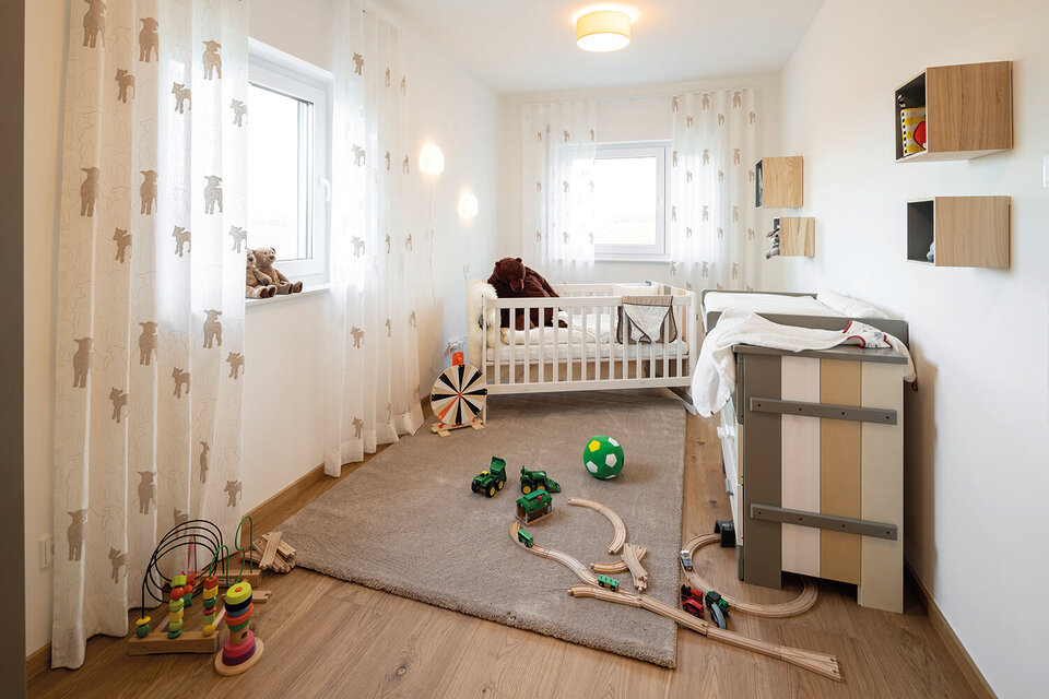 Helles Kinderzimmer mit weißem Babybett, Vorhängen mit Tiermotiven, Spielteppich und verteiltem Spielzeug.