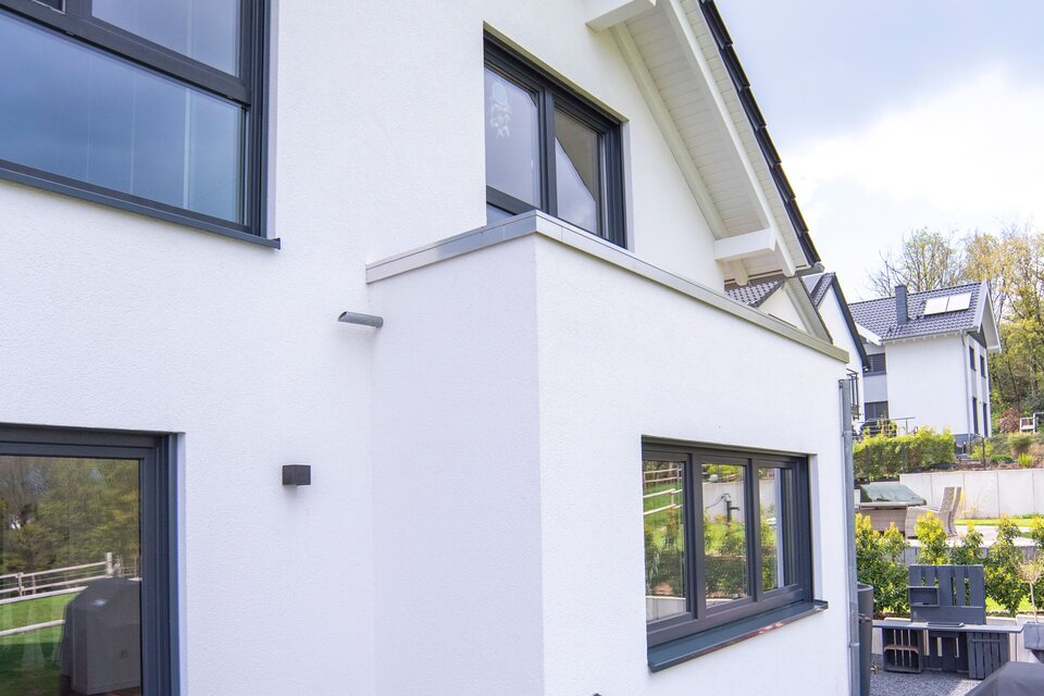 Moderne Terrasse eines frei geplanten FingerHaus mit grauen Bodenplatten, Sitzbereich und direktem Zugang zum Garten.