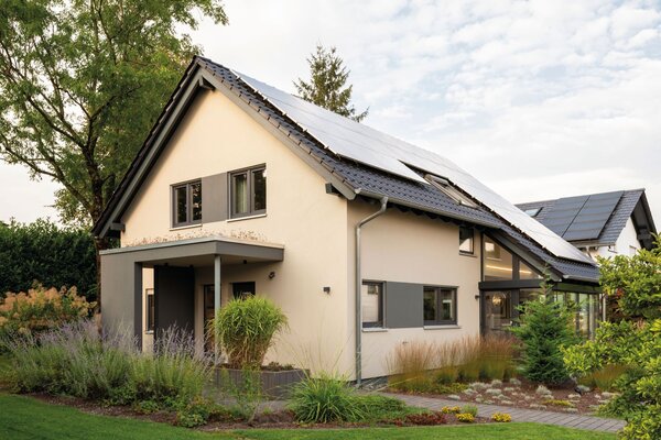 Modernes Musterhaus NEO in Wuppertal mit Eingangsüberdachung, Photovoltaikanlage auf dem Dach und gepflegtem Vorgarten im Abendlicht.