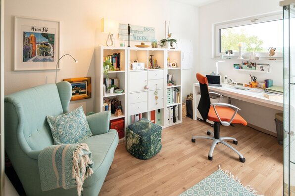 Helles Arbeitszimmer in einem frei geplanten FingerHaus mit Schreibtisch, ergonomischem Stuhl, Regalwand, gemütlichem Lesesessel und großen Fenstern.