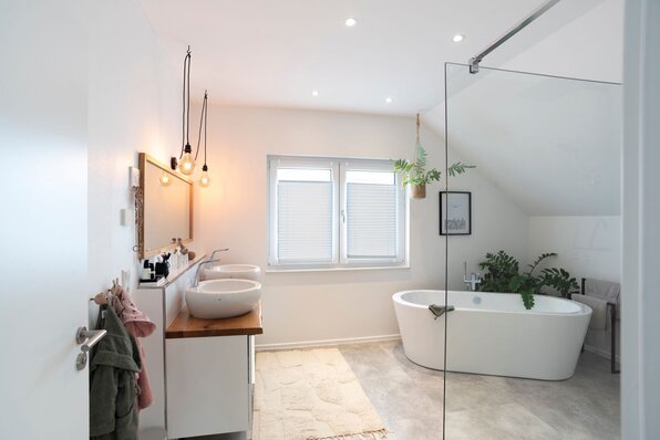 Modernes Badezimmer in einem FingerHaus-Haus mit freistehender Badewanne, Doppelwaschbecken auf Holzkonsole, Hängepflanzen und hellen Wandfarben unter der Dachschräge.