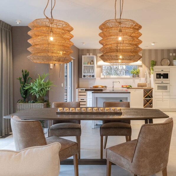Gemütlicher Essbereich im Musterhaus SENTO von FingerHaus in Bad Vilbel mit großem Holztisch, Lederstühlen, markanten Korbleuchten und angrenzender Landhausküche mit Vitrine.