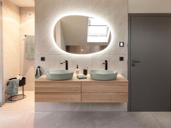 Modernes Badezimmer im Musterhaus JUNO 300 in Mülheim-Kärlich mit Doppelwaschtisch aus Holz, runden Aufsatzwaschbecken und beleuchtetem Spiegel.