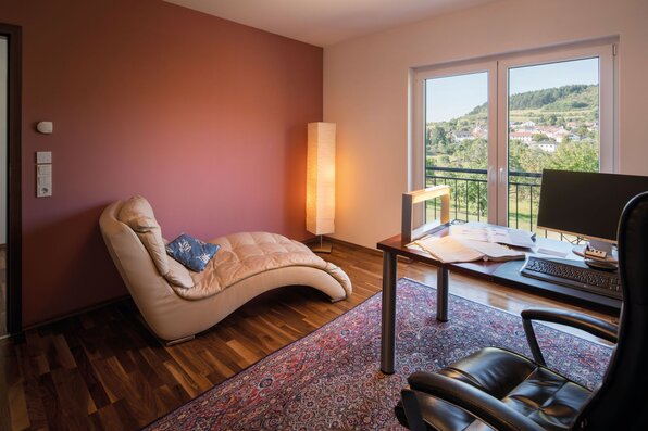 Helles Esszimmer in einem frei geplanten Finger-Haus mit großem Holztisch, braunen Stühlen, hellem Teppich, bodentiefen Fenstern und Zugang zur Terrasse.