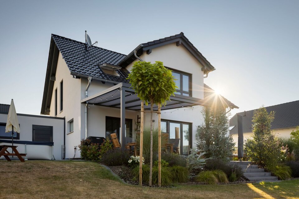 Außenansicht eines Einfamilienhauses SENTO 403 mit Satteldach, Terrassenüberdachung, Gartenanlage und tief stehender Sonne