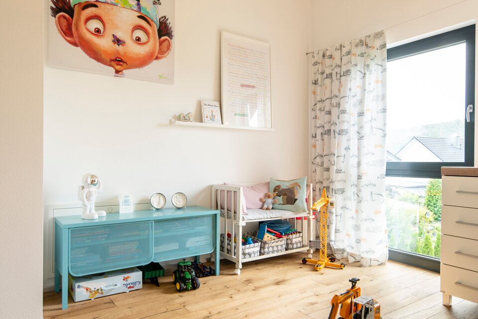 Freundliches Kinderzimmer mit Holzbalken, großem Fenster und farbenfroher Spielecke.