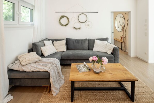 Gemütliches Wohnzimmer im frei geplanten FingerHaus mit grauer Sofalandschaft, Holztisch und moderner Deko.