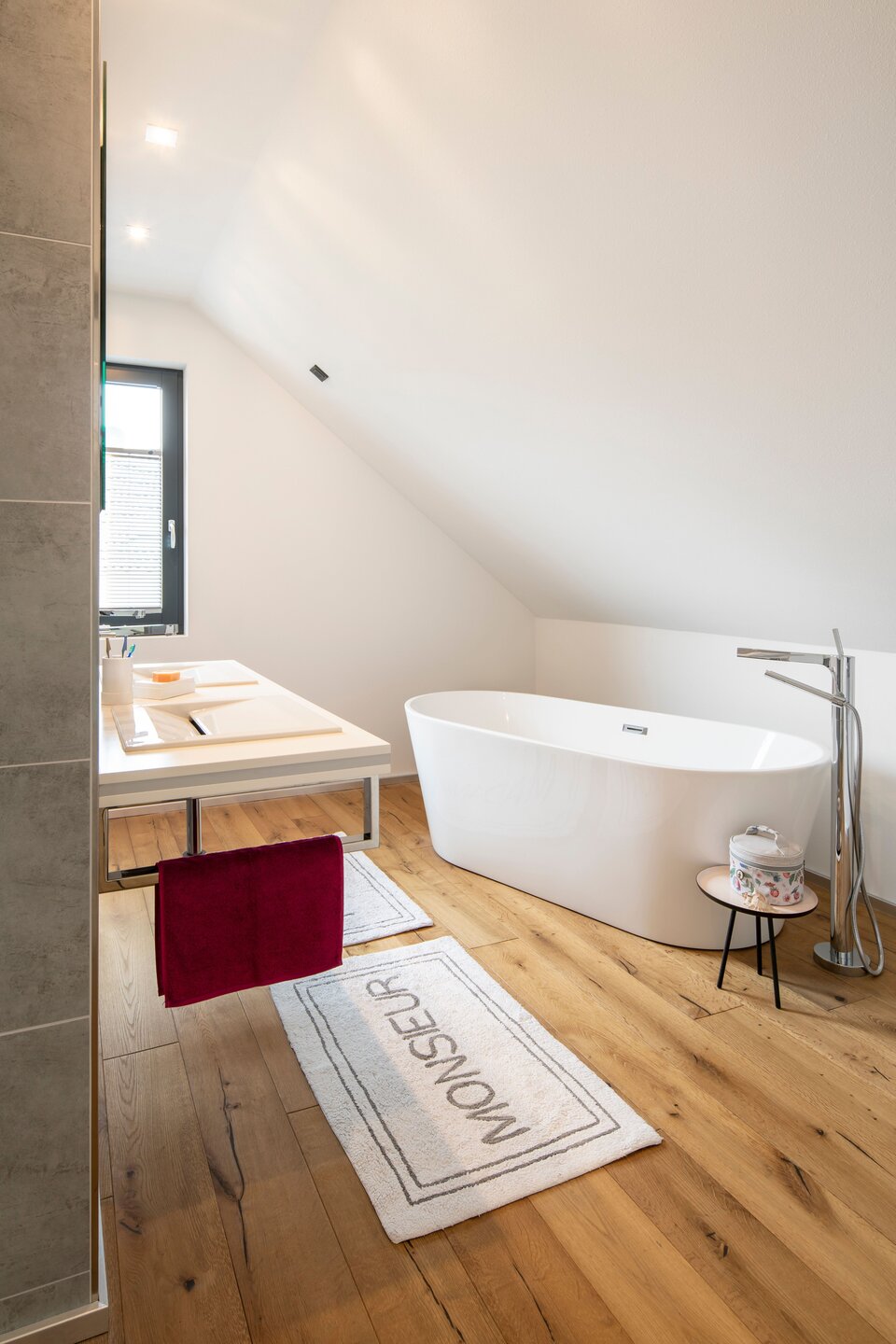 Großzügiges Badezimmer mit freistehender Badewanne, Waschbereich und Holzfußboden.