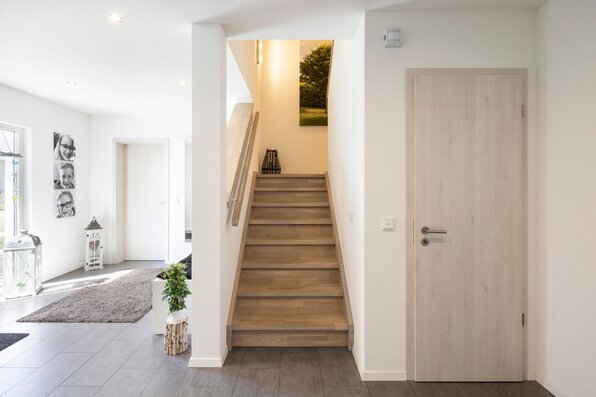 Heller Flur mit Holztreppe und moderner Innentür in einem frei geplanten Finger-Haus.