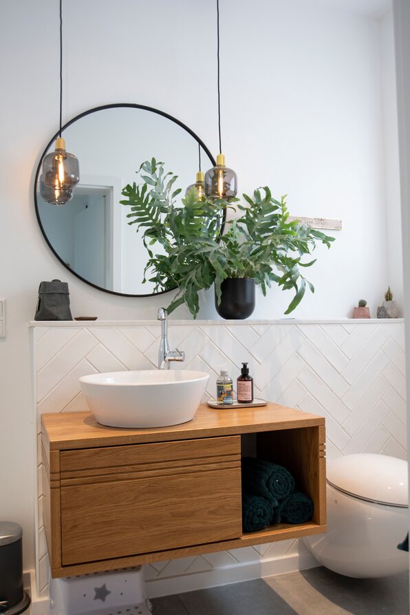 Modernes Gäste-WC in einem frei geplanten FingerHaus mit Holzwaschtisch, rundem Spiegel und stilvollen Hängelampen.