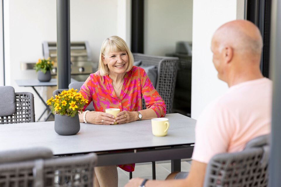 Ein Paar sitzt auf der Terrasse eines modernen Hauses und genießt gemeinsam eine Tasse Kaffee.