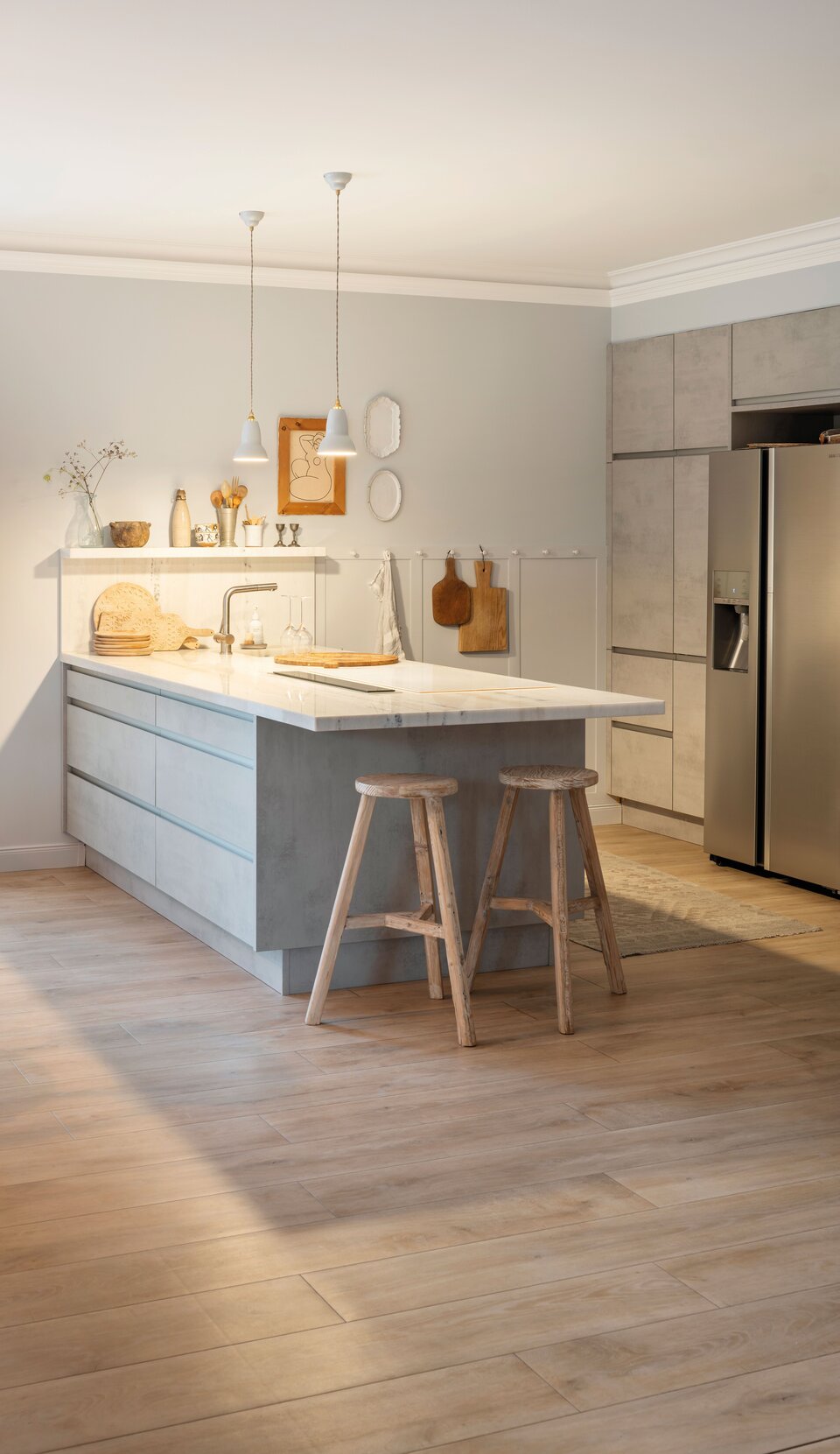 Helle Küche mit zentraler Kochinsel, Holzstühlen und großen Fenstern. Holzfußboden, Pendelleuchten und hell gestaltete Schränke schaffen ein warmes, modernes Ambiente.