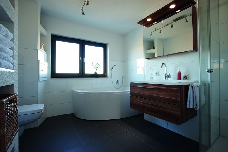 Modernes Badezimmer mit Eckbadewanne, Waschbecken und dunklem Boden.