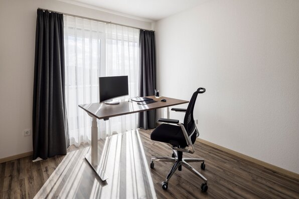 Modernes Homeoffice in einem FingerHaus mit Schreibtisch, Bürostuhl und großem Fenster mit Vorhängen.